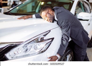 Visiting Car Dealership. Handsome Black Man Is Hugging His New Car And Smiling