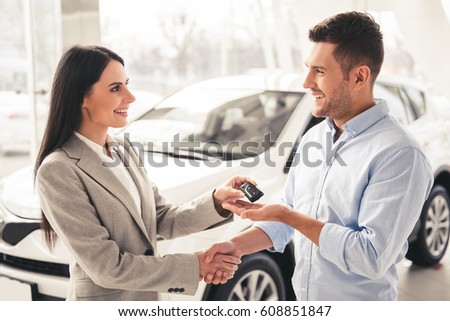 Visiting car dealership. Handsome man is getting car key from beautiful sales manager, shaking her hand and smiling