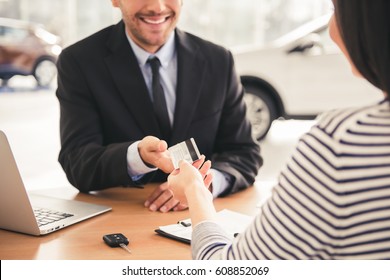 Visiting Car Dealership. Handsome Sales Manager Is Taking A Credit Card From The Client And Smiling