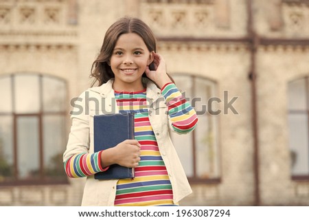 Visiting library can encourage reading and exploration in children. Interesting story for kid. Homework concept. Little girl hold book. Small girl with book urban background. Book from library