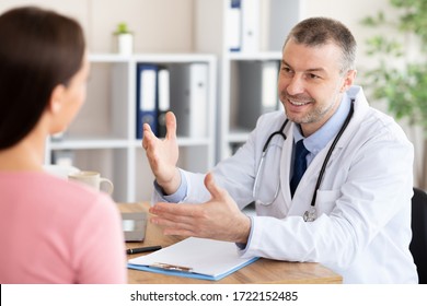 Visiting Physician. Cheerful Male Doctor Talking With Unrecognizable Patient During Appointment Sitting In Office