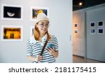 Visitor woman standing takes picture art gallery collection in front framed paintings pictures with mobile phone, Asian female watching at photo frame with smartphone at artwork gallery show