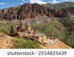 Visitors admire the ancient architecture of Noravank Monastery surrounded by stunning red rock formations.