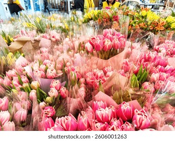 Visitors browse through an array of pink tulips and various flowers for sale at a lively market filled with colors and activity.