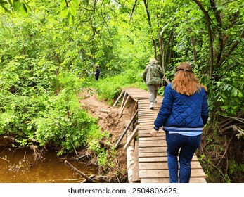 Visitors explore a serene forest path, walking on wooden bridge surrounded by vibrant greenery - Powered by Shutterstock