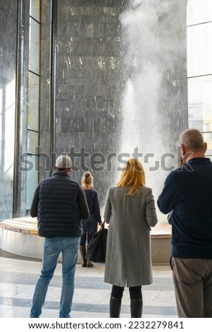 Visitors looking at, and perhaps drinking according to prescription, the free permanent hot spring on the famous covered promenade in the spa town of Karlovy Vary.