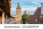 Visitors to Rothenburg ob der Tauber stroll through picturesque streets, admiring ancient towers and charming rooftops under a blue sky, soaking in the town