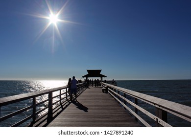 Visitors Stand On Landmark The Pier In Naples FL, Popular For Exquisite Sunsets And Boatless Fishing, As Blazing Sun Begins To Set In The Cloudless Blue Sky. Gulf Of Mexico. 