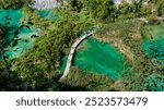 Visitors stroll along a wooden boardwalk, surrounded by lush greenery and vibrant turquoise waters, Plitvice Lakes in Croatia