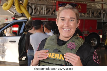 Vista, CA / USA - October 12, 2019: Friendly Young Female Police Officer Smiles For The Camera At Fire Station Open House, As Families Explore The Cruiser.                              