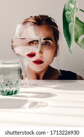 Visual Concept. Fashion Woman Portrait, Eye Looks Through The Glass Of Water. Object Distortion, Optical Illusion. Green, White, Red. Minimalistic Contemporary Art.Beautiful Woman's Face In Wine Glass