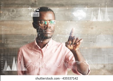 Visual effects. Future technology touch screen interface. Handsome African American businessman in shirt touching screen interface, drawing a chart in futuristic office. Selective focus on the hand