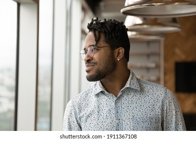 Visualizing Success. Head Shot Of Confident Stylish Young Afro American Man Wearing Glasses Looking At Window Thinking Happy Thoughts. Smiling Black Hipster Guy Student Businessman Imagine Good Future