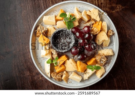 A visually appealing cheese platter featuring various cheese types, fresh grapes, and a small bowl of dark dip, garnished with mint leaves for added freshness.