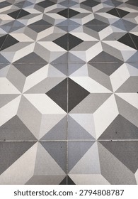 A visually engaging floor composed of ceramic tiles arranged in a captivating geometric pattern creating an illusion of three-dimensional cubes and pyramids using various shades of gray white and black.