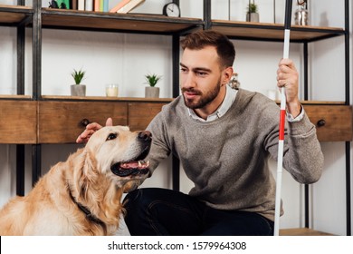 Visually Impaired Man With Walking Stick Stroking Golden Retriever At Home