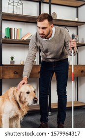 Visually Impaired Man With Walking Stick Stroking Golden Retriever At Home