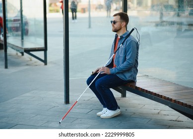 Visually impaired man with walking stick, sitting on bench in city park. Copy space. - Powered by Shutterstock