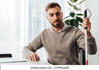 Visually Impaired Man In Wireless Earphones Holding Walking Stick At Table