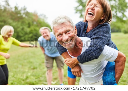 Vital seniors play together in the park in the summer and ride piggyback