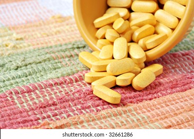 Vitamin B capsules spilling from small dish onto pastel placemat.  Macro with shallow dof.  Focus on front vitamin.