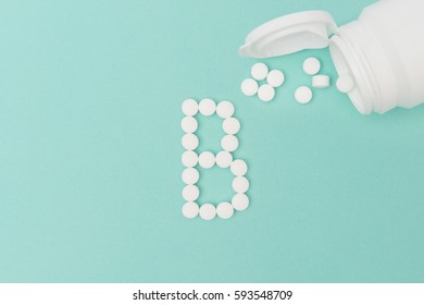 Vitamin B pills forming the letter 'B' with toppled medicine bottle over turquoise background
