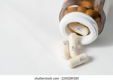 Vitamin B3. Vitamins in capsules. White capsules with vitamin B3, niacinamide or nicotinic acid are scattered on the table from a bottle on a white background. Dietary supplements in tablets.