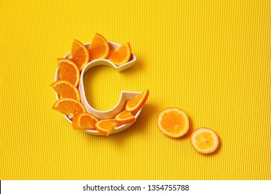 Витамин С в концепции питания. Тарелка в форме буквы C с оранжевыми ломтиками на ярко-желтом фоне. Аскорбиновая кислота важна для работы иммунной системы.