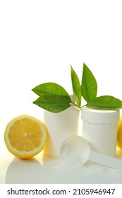  Vitamin C Powder, White Measuring Spoon, White Jar And Lemon In A Cut With Green Leaves Isolated On White Background. 