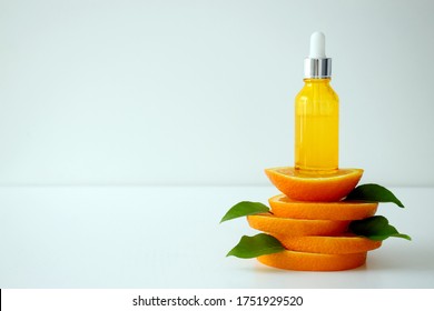 Vitamin C serum in cosmetic bottle on top of orange citrus slices with green leaves on white background. Citrus essential oil, cosmetics aromatherapy. Organic SPA cosmetics with herbal ingredients.