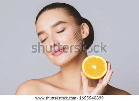 Vitamin C for skin. Delighted young pretty woman with closed eyes holding orange half over grey background