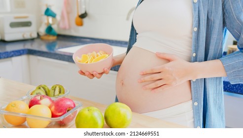 Vitamin C supplementation for Pregnancy - close up of asian pregnant woman holding a bowl with oranges is touching her belly and there are fruits or vegetable on table in kitchen at home - Powered by Shutterstock