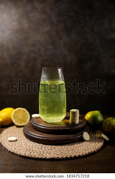 Vitamin C tablets. A glass with an\
effervescent tablet on a wooden stand. Dark\
photo.