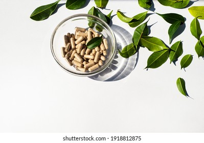 Vitamin capsules in a glass cup. Trace elements and health supplements. Glass shadow and fresh leaves. Copy space for text. White background.