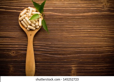 Vitamin capsules in a wooden spoon on a wooden background.