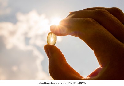 Vitamin D keeps you healthy while lack of sun. Yellow soft shell D-vitamin capsule against sun and blue sky on sunny day. Cure concept. - Shutterstock ID 1148454926