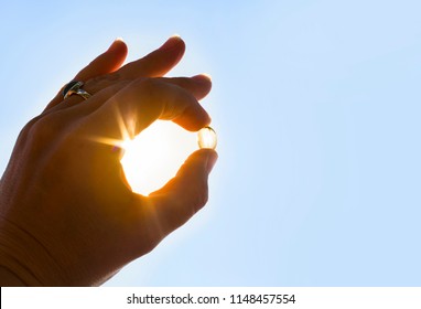 Vitamin D keeps you healthy while lack of sun. Hand holding yellow soft shell fish oil capsule against sun and blue sky on sunny day.  - Shutterstock ID 1148457554