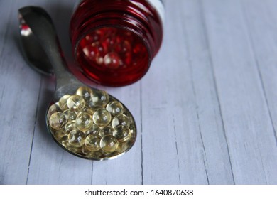 Vitamin D Pills On A Spoon, Red Container, Wooden Background