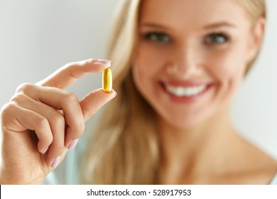 Vitamin And Supplement. Beautiful Smiling Woman Holding Fish Oil Capsule In Hand. Portrait Of Happy Girl Taking Pill With Cod Liver Oil, Omega-3. Diet Nutrition And Healthy Eating Lifestyle Concept.
