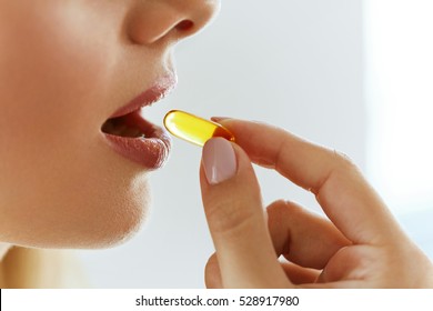 Vitamin And Supplement. Closeup Of Beautiful Young Woman Taking Yellow Fish Oil Pill. Female Hand Putting Omega-3 Capsule In Mouth. Healthy Eating And Diet Nutrition Concepts. High Resolution Image