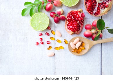 Vitamin supplements on wooden spoon with healthy fruits berry, lime, pomegranete on white wooden background.Top view.