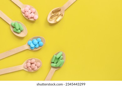 Vitamins on a yellow background, top view. Pills of different colors in wooden spoons, flat lay. Medicines, vitamins and dietary supplements
