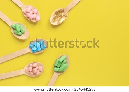 Vitamins on a yellow background, top view. Pills of different colors in wooden spoons, flat lay. Medicines, vitamins and dietary supplements