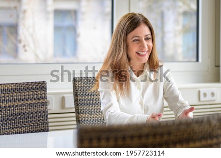 Vivacious animated woman gesturing with her hand and laughing as she sits at a conference table in a high key office or apartment with window backdrop