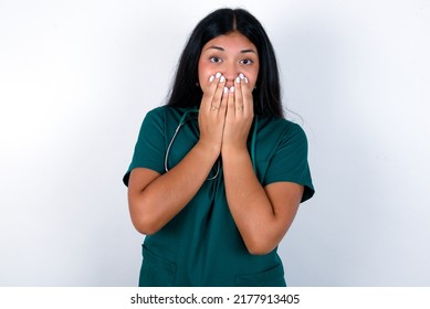 Vivacious Doctor Hispanic Woman Wearing Surgeon Uniform Over White Background , Giggles Joyfully, Covers Mouth, Has Natural Laughter, Hears Positive Story Or Funny Anecdote