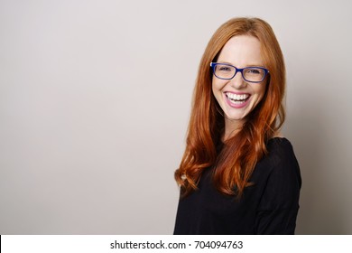 Lebhafte junge Rothaarige mit Brille, die mit einem strahlenden Lächeln mit Kopienraum über die Kamera lacht