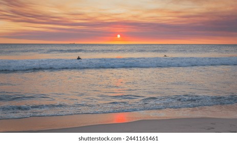 Vivid beautiful sunset orange smoke affected clouds over beach with two surfers looking toward the horizon - Powered by Shutterstock