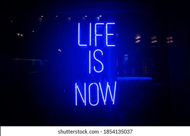 Vivid Blue Neon Sign About Life. Life Is Now Motivation. Urban City Light Window With Bright Signboard Isolated On Black.