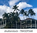 Vivid blue sky splashed with bright white clouds behind windblown palm trees above the historic Plantation Inn in old Lahaina, Maui. 