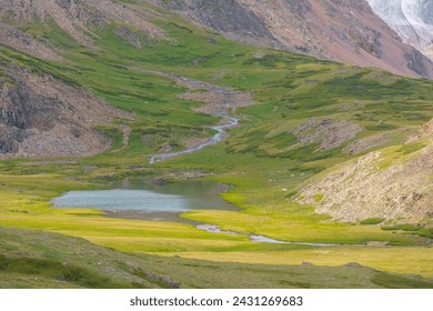 Vivid green landscape with beautiful alpine lake and mountain river close up. Small mountain lake and creek in sunny green valley. Water stream and on steep hillside in sunlight. Ripples on lake water - Powered by Shutterstock